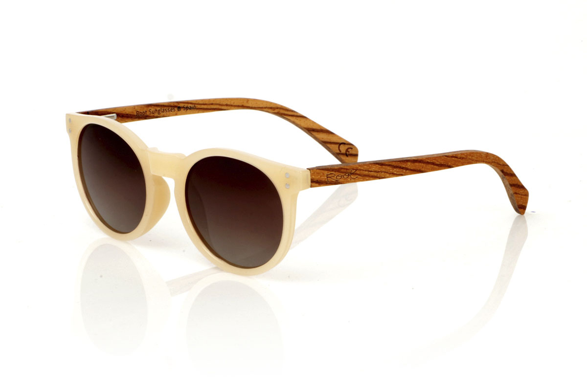 Wood eyewear of Zebrano modelo INKY. INKY sunglasses capture the essence of a delicate and feminine design with their rounded shape and smaller size. The frame in a sophisticated satin-gloss ivory offers a touch of light and elegance, while the zebrawood temples introduce a natural and striking contrast. This model is ideal for those looking for distinctive but subtle glasses that complement without overloading. With measurements of 138x48mm and a caliber of 47, the INKY adapts perfectly to thinner faces, ensuring comfort and style. Immerse yourself in the beauty of the details to enhance your look with a unique charm. | Root Sunglasses® 